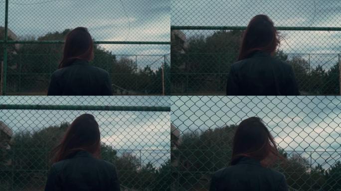 一个穿着机车夹克的美丽而热情的女孩正在走路。年轻女子背在金属栅栏格子上的框架里。
