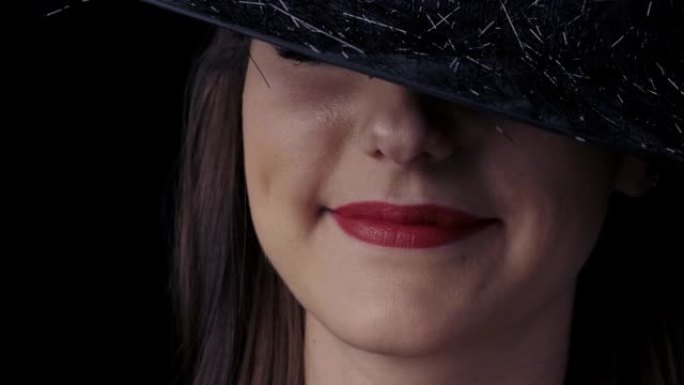 一个戴着黑色巫婆帽子的迷人神秘女人的半侧脸特写，鲜红的嘴唇微笑着。万圣节概念。