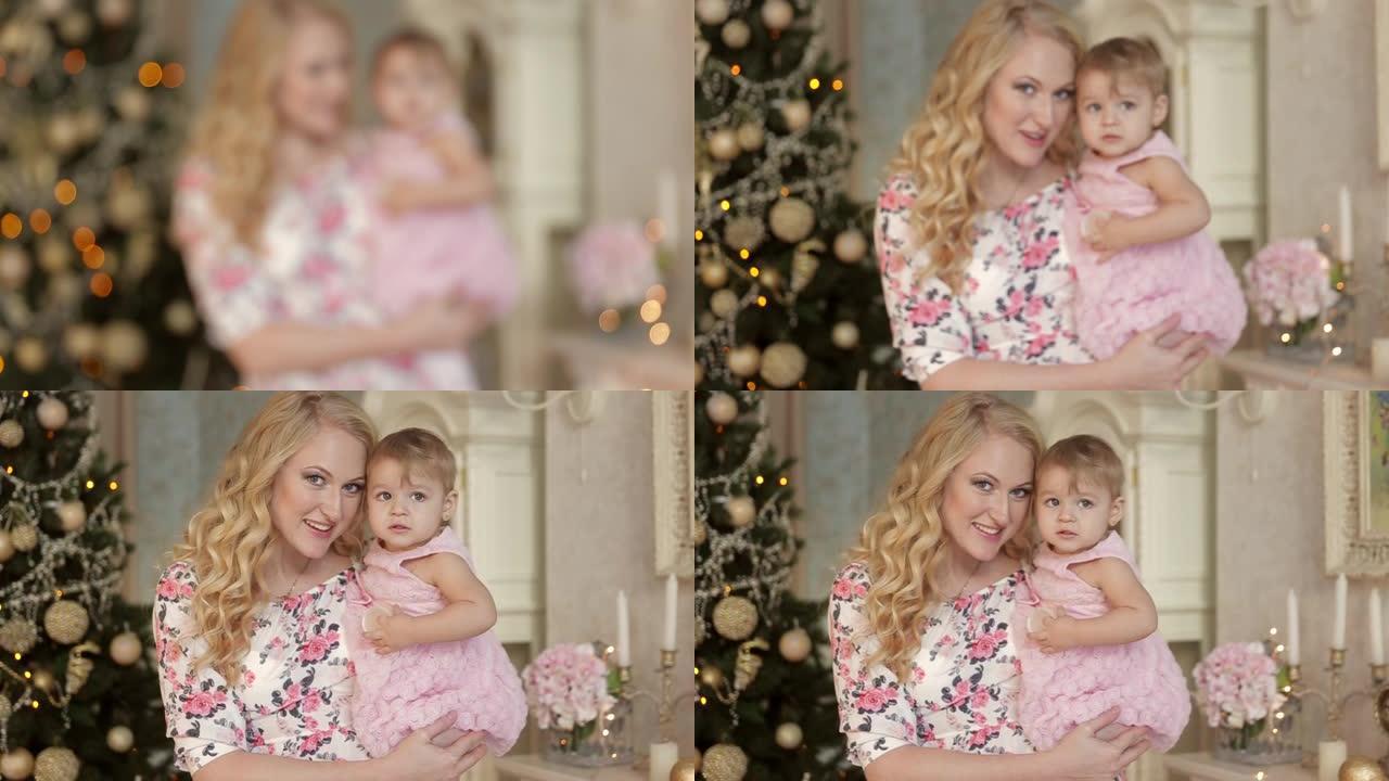 年轻母亲的肖像手拿2岁的小女儿，在装饰圣诞树的背景下，看着相机微笑。新年和平安夜
