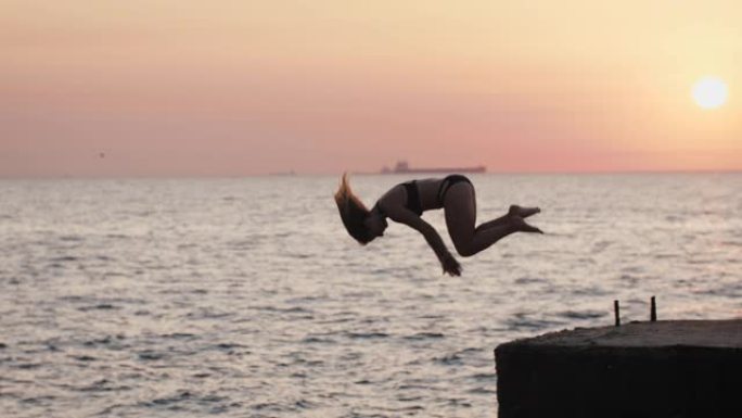 年轻的尤曼从海上码头跳下来，在美丽的日出时做前空翻，慢动作