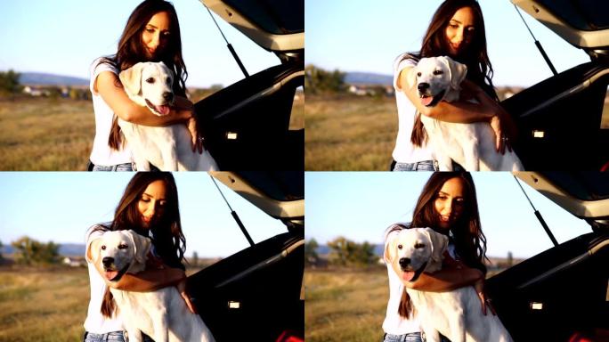 年轻漂亮的女人把她的狗抱在汽车后备箱上