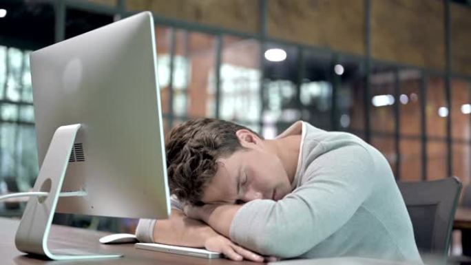 疲惫的年轻人在办公桌前小睡一会儿