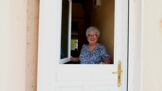 老年妇女打开房子的前门，欢迎家里的人