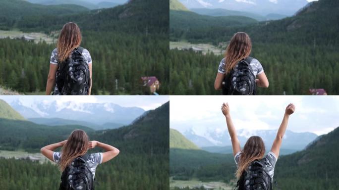 穿着短裤背包的女孩旅行者站在山顶，举起手来。目标达成。慢动作