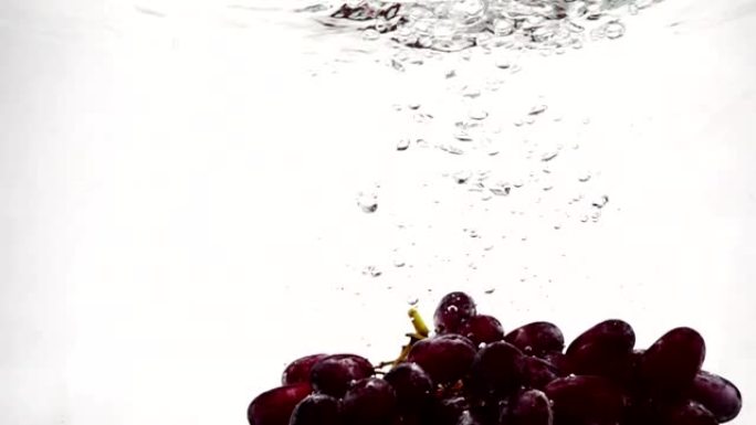 慢动作的红葡萄。一束葡萄浸泡在带有气泡的水中。