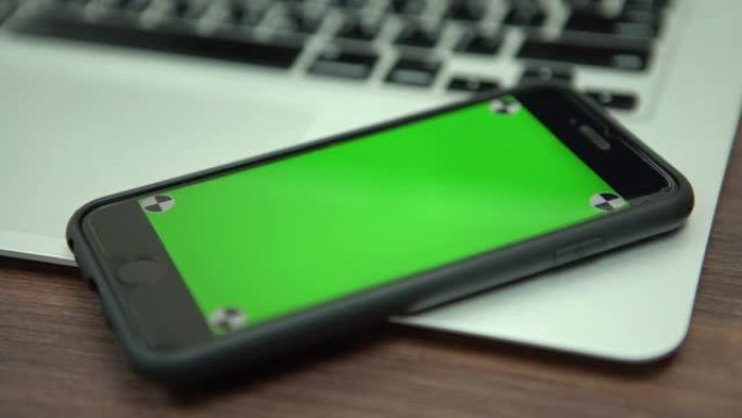 绿色屏幕手机靠近笔记本电脑的4k特写镜头。带智能手机的电脑