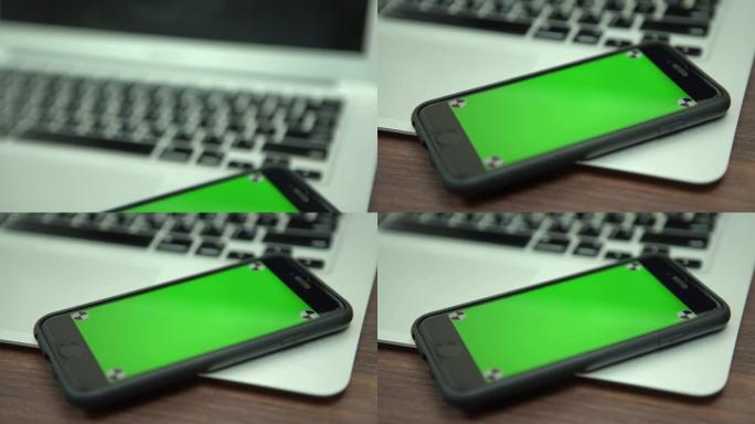 绿色屏幕手机靠近笔记本电脑的4k特写镜头。带智能手机的电脑