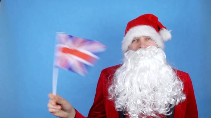 一个穿着圣诞老人服装留着胡子的男人在蓝色背景上挥舞着大不列颠的旗帜。世界各地的新年假期概念