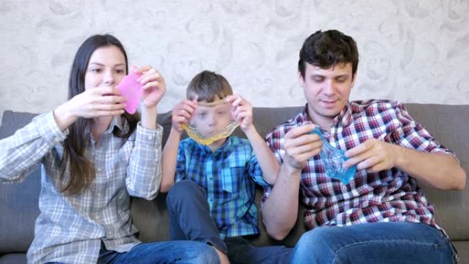幸福的家庭妈妈，儿子和爸爸，坐在沙发上玩史莱姆。