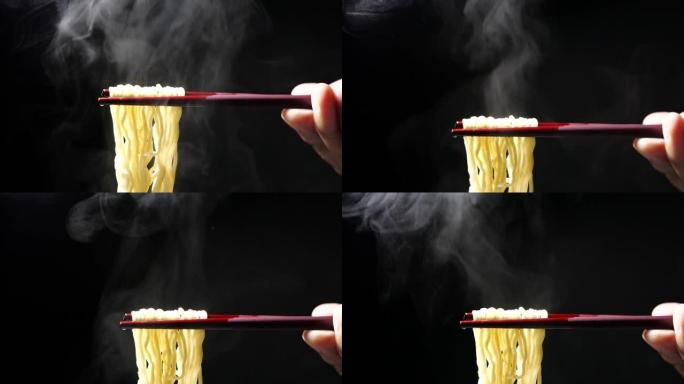 在慢动作，垃圾食品和快餐概念，亚洲餐特写镜头中，用筷子在黑色背景的碗里放蒸汽和烟的美味面条