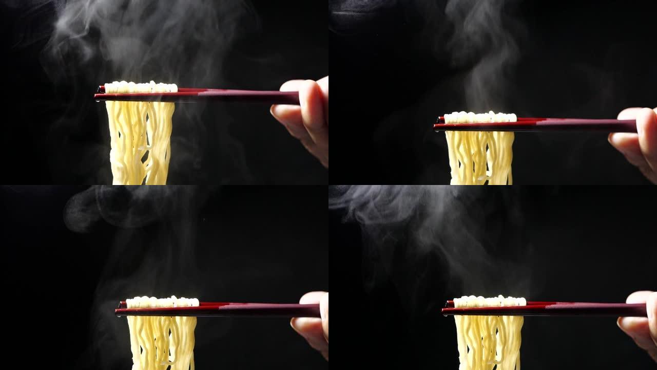 在慢动作，垃圾食品和快餐概念，亚洲餐特写镜头中，用筷子在黑色背景的碗里放蒸汽和烟的美味面条