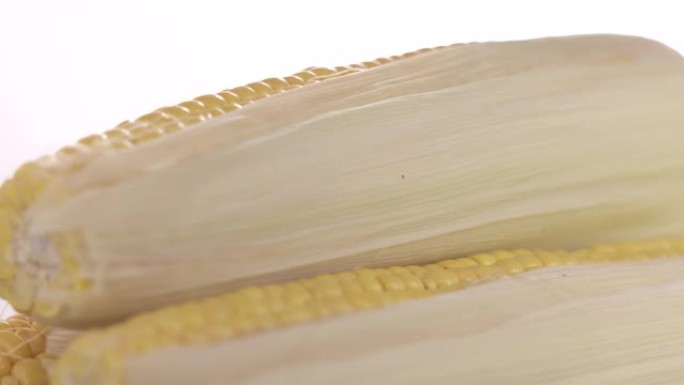 新鲜的生甜玉米棒在白色背景上旋转特写。