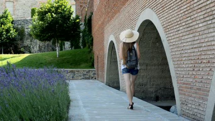 戴着帽子的年轻女子沿着古老的墙壁行走并抚摸她