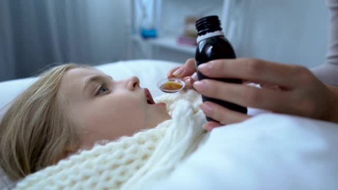 有爱心的女性父母给躺在床上的生病的小女儿咳嗽糖浆，流感