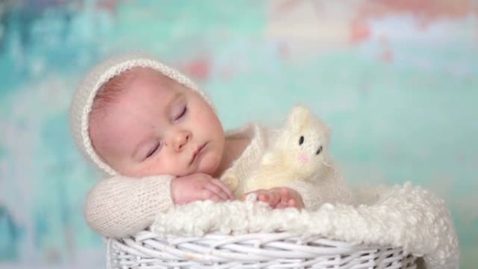 可爱的小男孩，整体穿着手工编织的白色泰迪熊，带着篮子里的小针织玩具睡得很漂亮