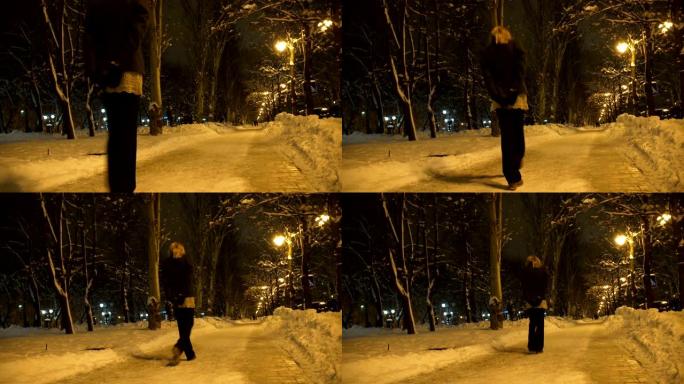 孤独的年轻女子晚上在白雪皑皑的冬季城市公园里散步，灯光下的黄光