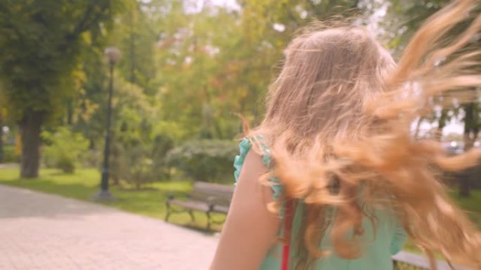 特写镜头后视图年轻可爱的女性在公园里走路转身看着相机，头发讨人喜欢地微笑着