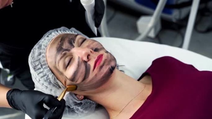 特写美容师将黑碳面膜应用于女性面部皮肤