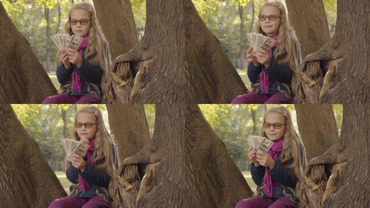 年轻的金发高加索女孩戴着光致变色眼镜数钱，想着坐在秋天公园或森林里的树上。青少年决定如何花她的零花钱