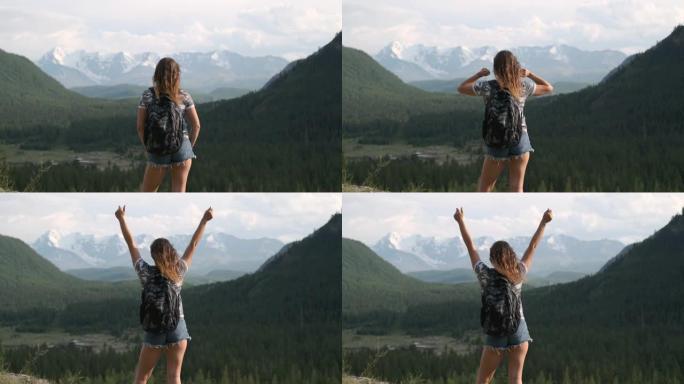 穿着短裤背包的女孩旅行者站在山顶，举起手来。目标实现