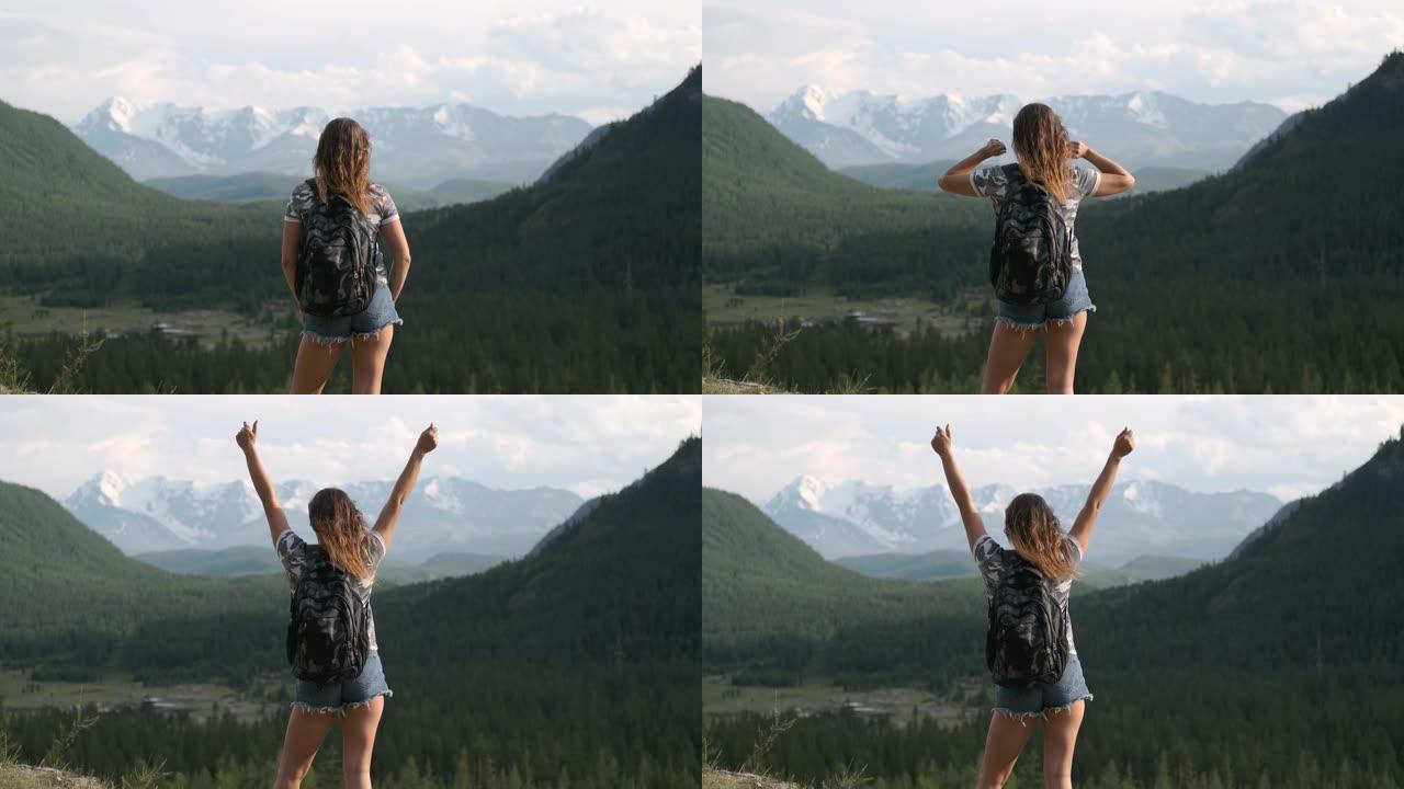 穿着短裤背包的女孩旅行者站在山顶，举起手来。目标实现