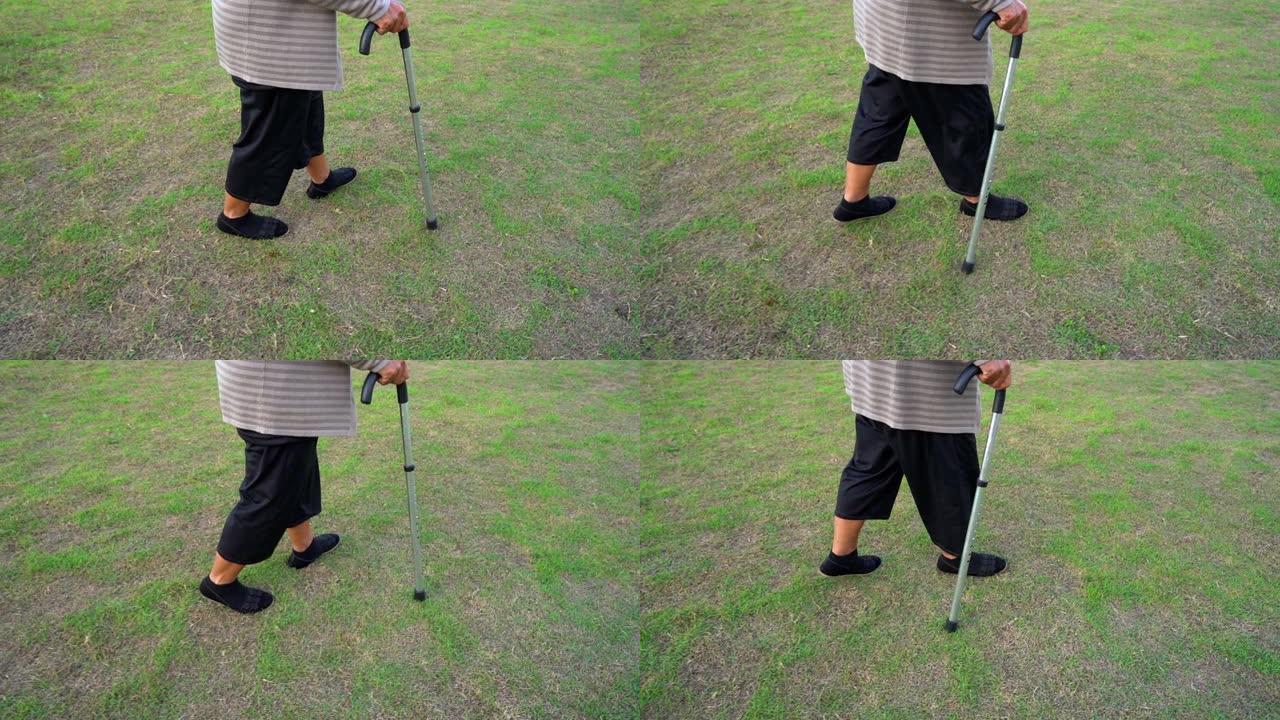 在草地上用手杖走路的高级女性腿的慢速运动