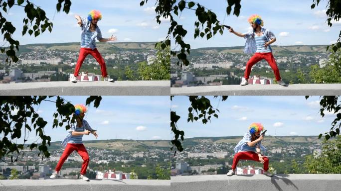 疯狂的哑剧手拿枪在栏杆上跳舞。在城市的背景下，一个带着手枪的小丑的有趣动作。