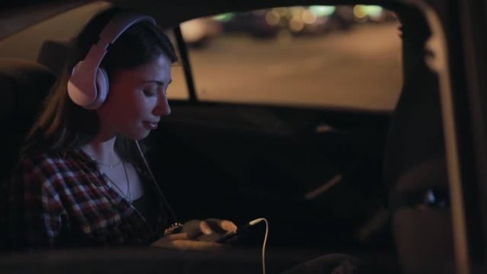 女乘客戴着立体声耳机在汽车上听音乐