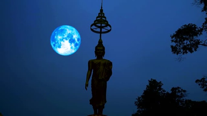 蓝色的收获月亮在夜空和剪影佛像上移动