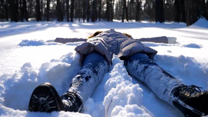 穿着冬装的年轻女孩躺在白雪皑皑的草地上，做天使。快乐的女人在雪地里玩耍，享受冬天的时光。开朗的女士在