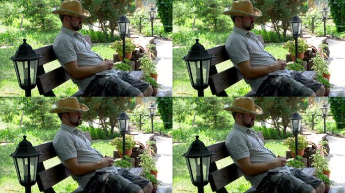 一个戴着草帽的男人睡在花园里的长凳上