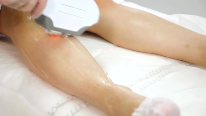 女性双手在医疗中心的凝胶腿上涂抹凝胶和滑动激光头