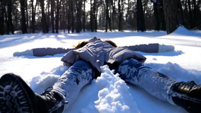 穿着冬装的年轻女孩躺在白雪皑皑的草地上，做天使。快乐的女人在雪地里玩耍，享受冬天的时光。开朗的女士在