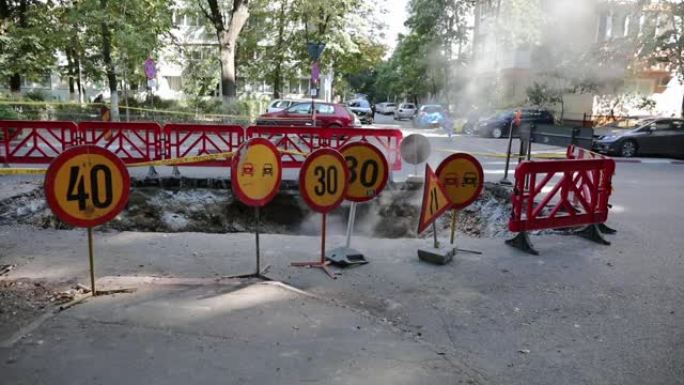 道路交通警告标志和沥青上的一个大洞周围的塑料围栏，蒸汽从那里出来