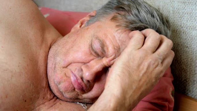 未刮胡子的老人睡在枕头上的床上，大声打鼾。