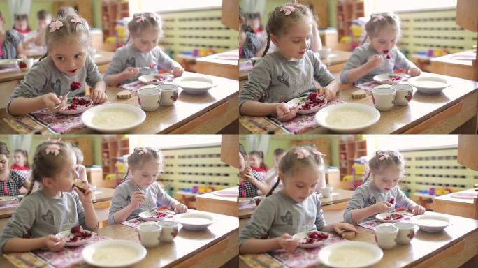 双胞胎女孩坐在幼儿园的餐桌旁吃沙拉。在学龄前嫉妒中吃饭。