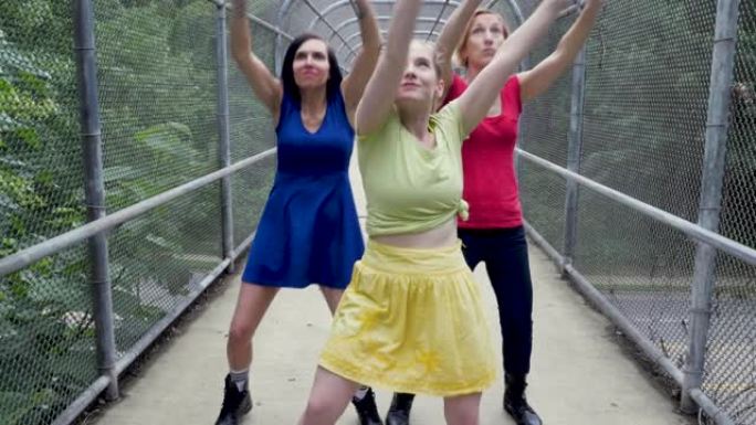 三个女人在被树木环绕的有盖人行天桥上向后跳舞
