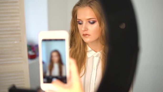 化妆师在手机上给模特拍照。深色嘴唇，灰色背景。化妆