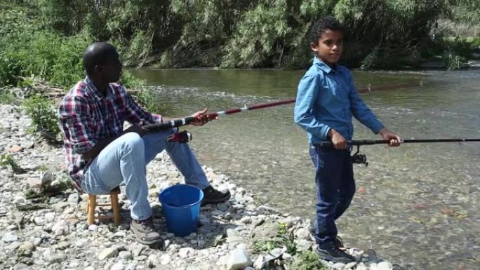 非洲男孩和他的父亲在河上用钓竿钓鱼