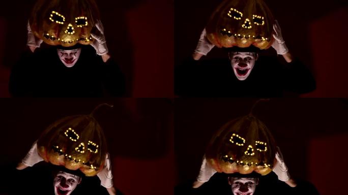 小丑化妆的吓人人拿着万圣节的南瓜，戴在头上。可怕的小丑在头上戴上南瓜形状的面具。可怕的小丑手里拿着一