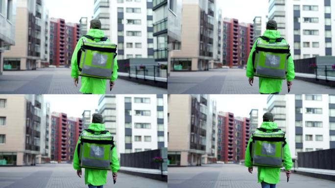 后面的镜头是年轻的男性食品快递员穿着绿色制服走在街上，带着隔热背包运送食物，手里拿着手机