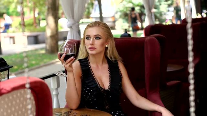 穿着裙子的漂亮女孩坐在夏日街头的咖啡馆里喝着红酒。