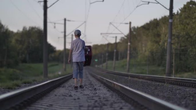 带旅行袋的有趣男孩在户外乘火车