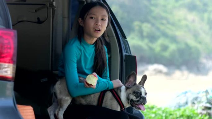 小女孩坐在车后座吃苹果和她的小狗。
