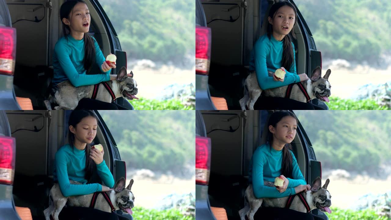 小女孩坐在车后座吃苹果和她的小狗。