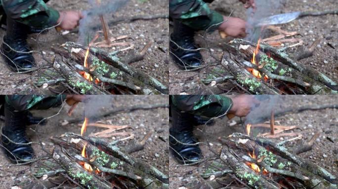 身着迷彩服的士兵用露营刀在露营区生火做饭的4K中拍摄。燃烧的火焰在雨林露营营火。