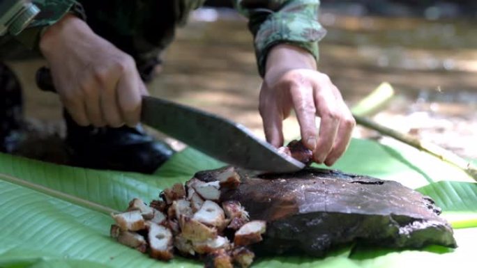在溪边的森林露营区，身着迷彩服的士兵用野营刀在天然木砧板上切烤烤烤肉的4K中拍摄。