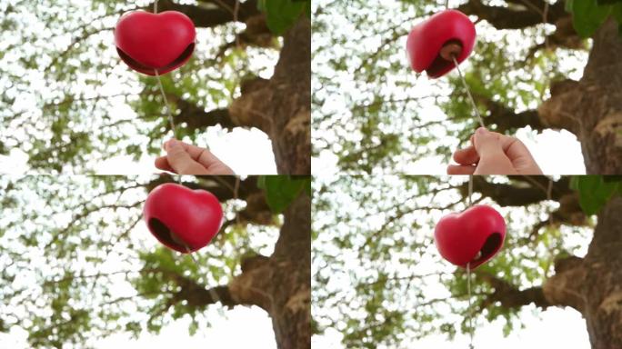 女人抓住了挂在花园里树枝上的红色心形陶瓷风铃。