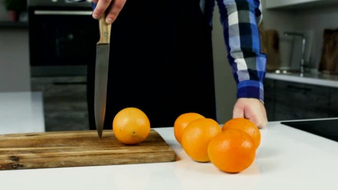 橘子在现代厨房的桌子上。一个穿着围裙的丰满男人看起来像厨师在木砧板上插刀。