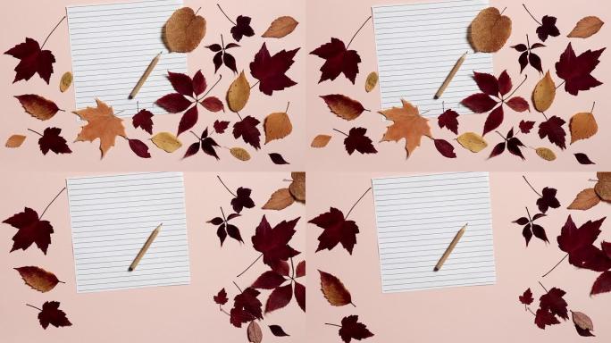 空纸与铅笔和粉红色背景上的彩色秋叶。风吹走了树叶。返校的概念